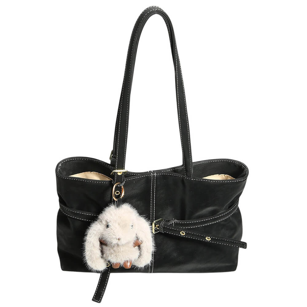A tan faux-leather tote bag with dual shoulder straps, a front strap detail with gold-tone rivets and buckle, and a white fluffy bunny plush keychain hanging from a ring.